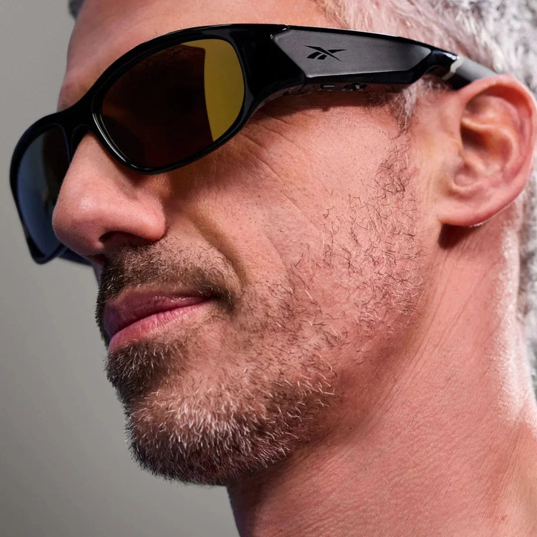 rimer plano de hombre con barba usando gafas deportivas Reebok negras con lentes amarillas de alto contraste.