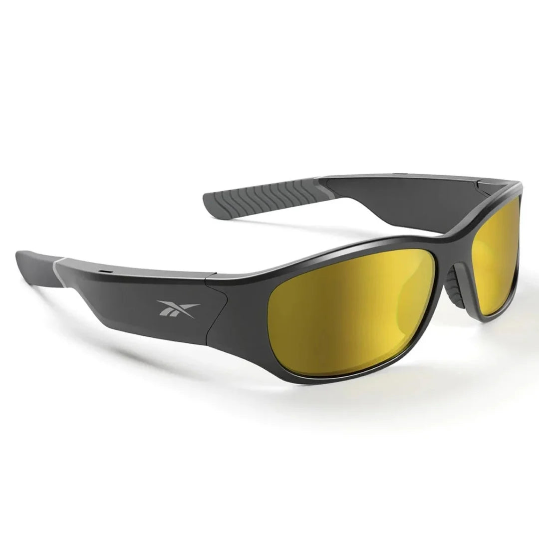 Gafas deportivas Reebok negras con lentes ámbar de alto contraste; vista en ángulo mostrando el logo y agarre en la patilla.